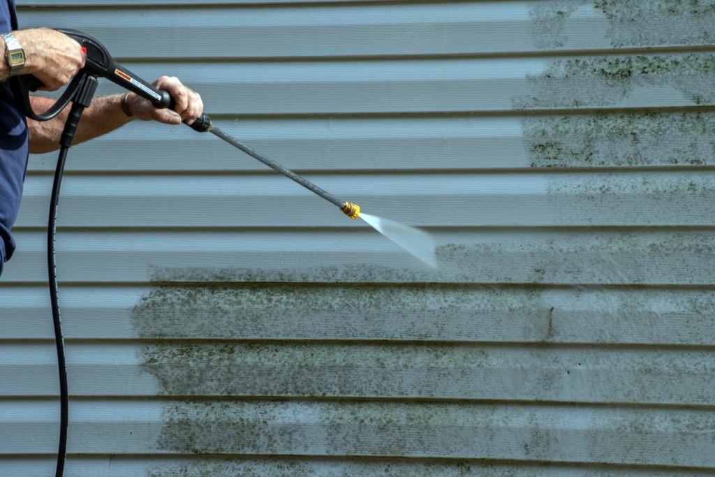 Worker power washing dirty exterior house siding pressure wash a house before painting