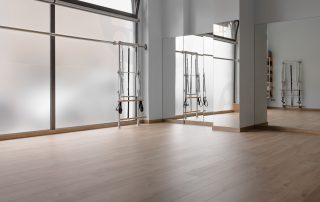 Pilates studio corner with wooden floors, a large window, a mirror and a pilates machine commercial painting