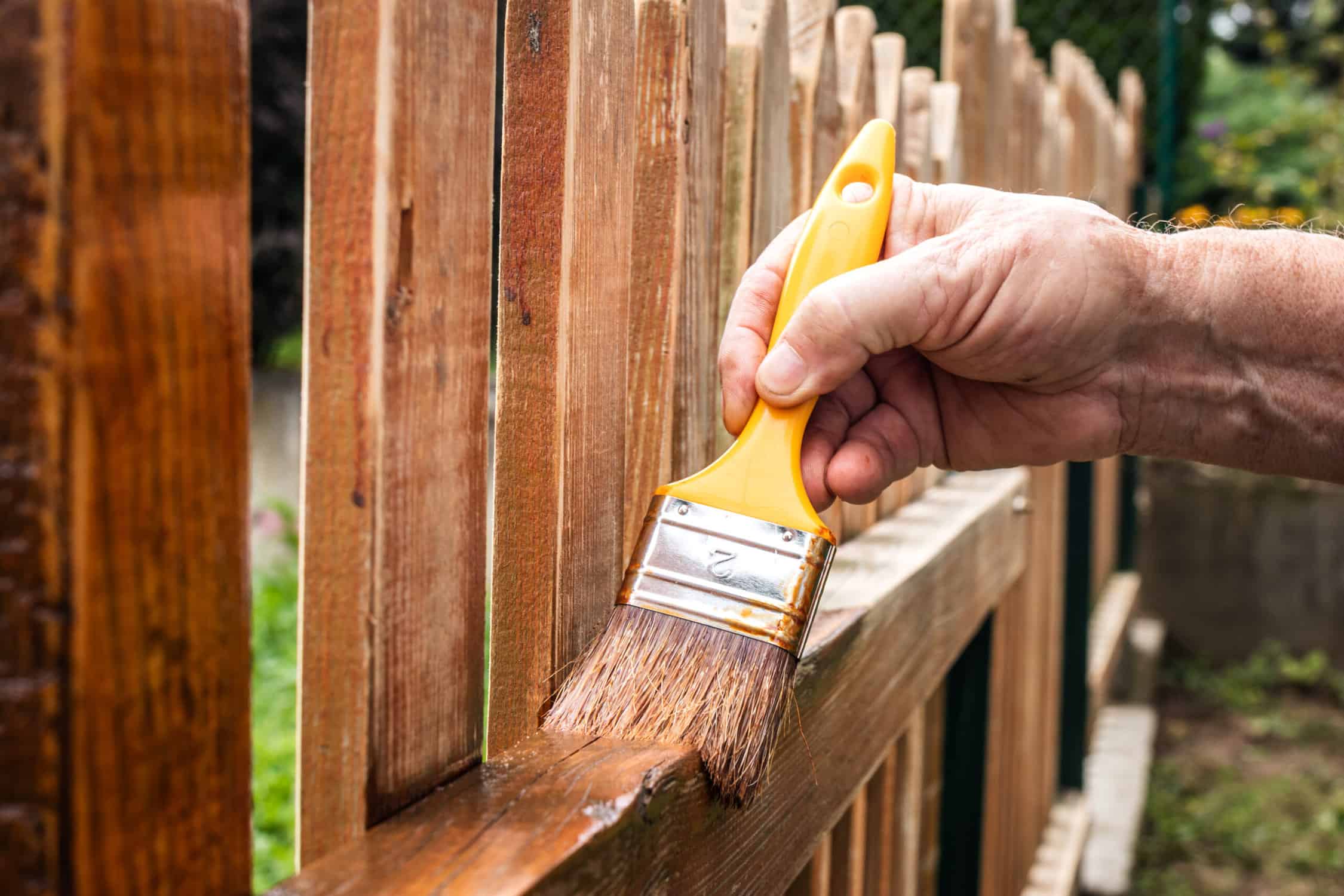 Painter painting picket fence with wood stain