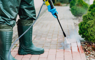 Man pressure washing red, conrete pavement block using high pressure water cleaner.