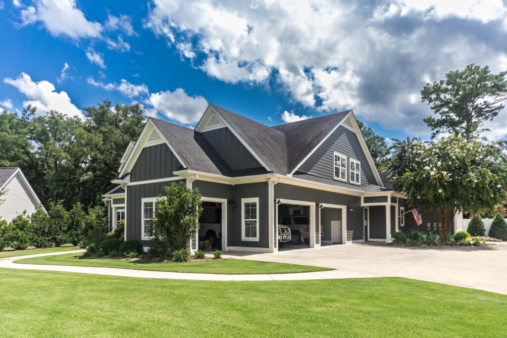 The side view of a large gray new construction house with a landscaped yard a three car garage and driveway how to dispose of paint